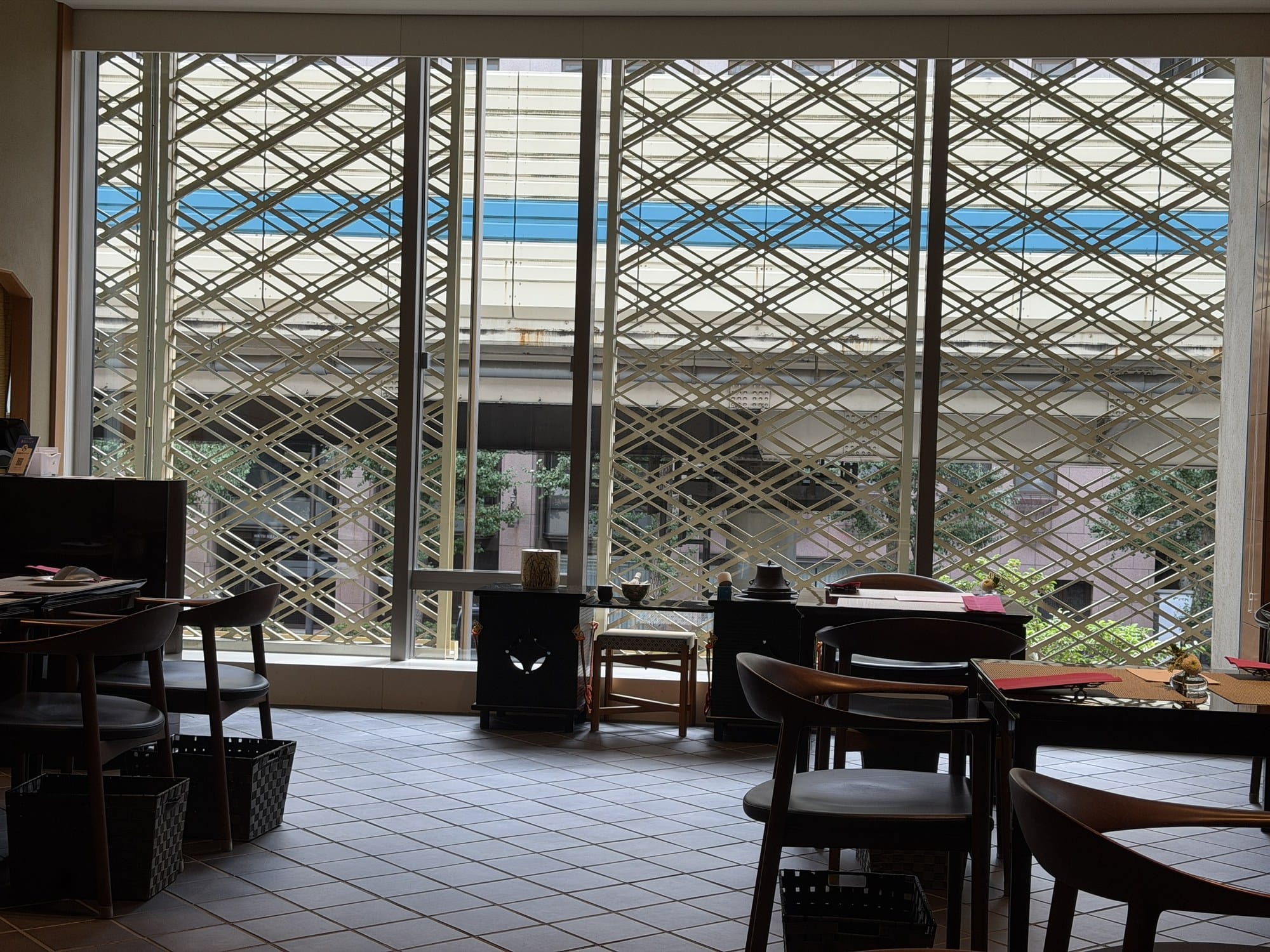 Detail of a white-wood kumiko lattice window in a diamond pattern, with Tokyo's elevated expressway visible through the gaps
