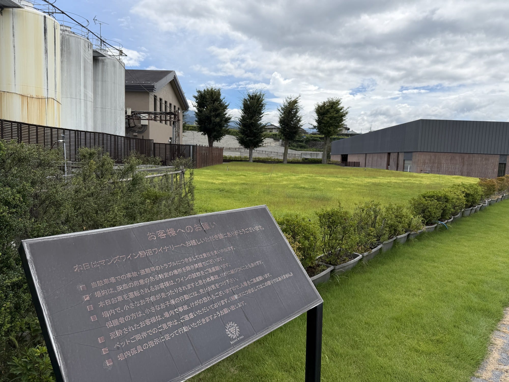 A metal notice board on the lawn at Manns Wines Katsunuma listing requests to visitors in Japanese