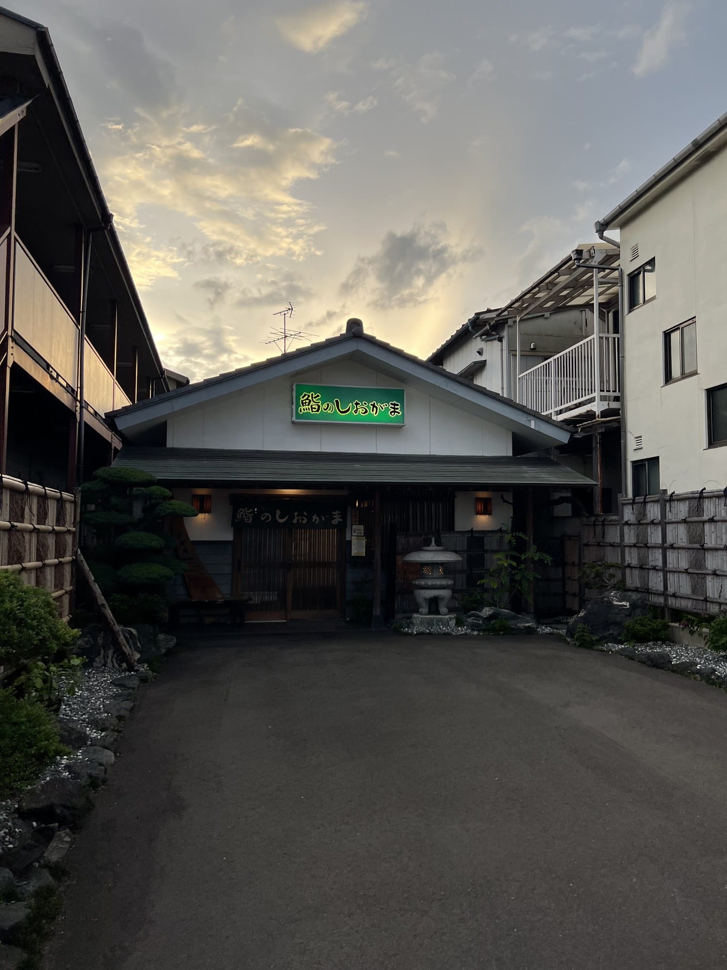 The wooden entrance of Sushi no Shiogama sushi restaurant in Shiogama, with stone lanterns and low plantings by the door