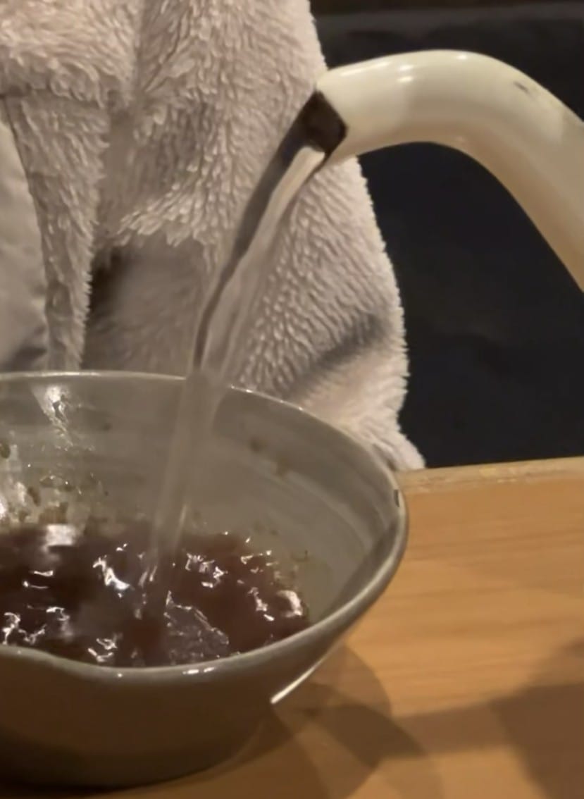 Soup being poured from a kettle into a bowl of leftover dipping sauce at Chame in Otaru