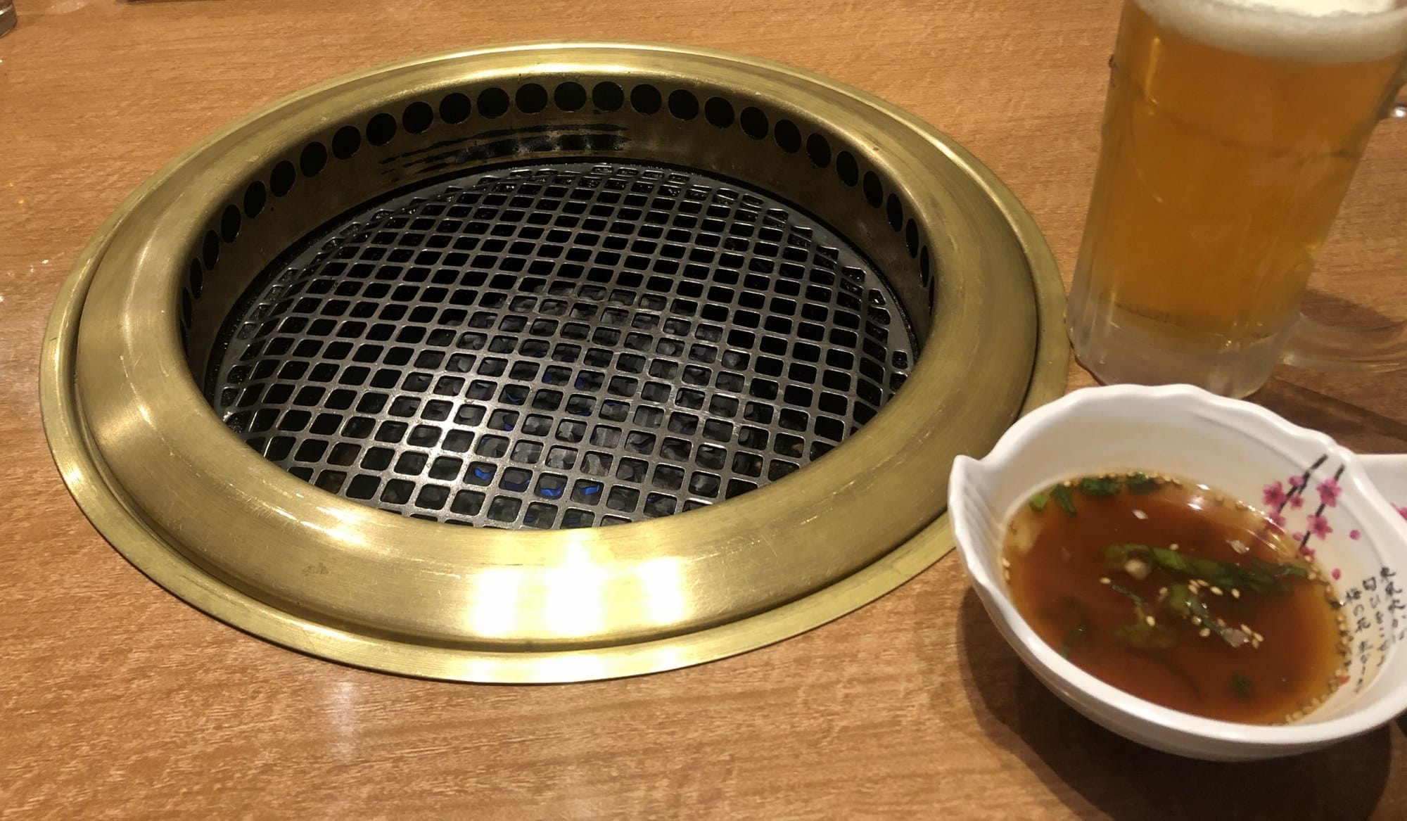 A tabletop grill, a beer and a bowl of tare dipping sauce with scallion and sesame at Daijinmon in Otaru