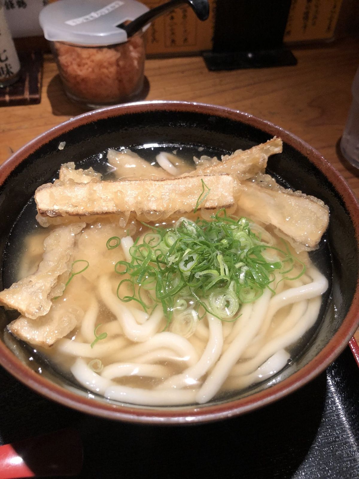 Bowl of kitsune udon with fried tofu puffs and green onions in clear dashi broth