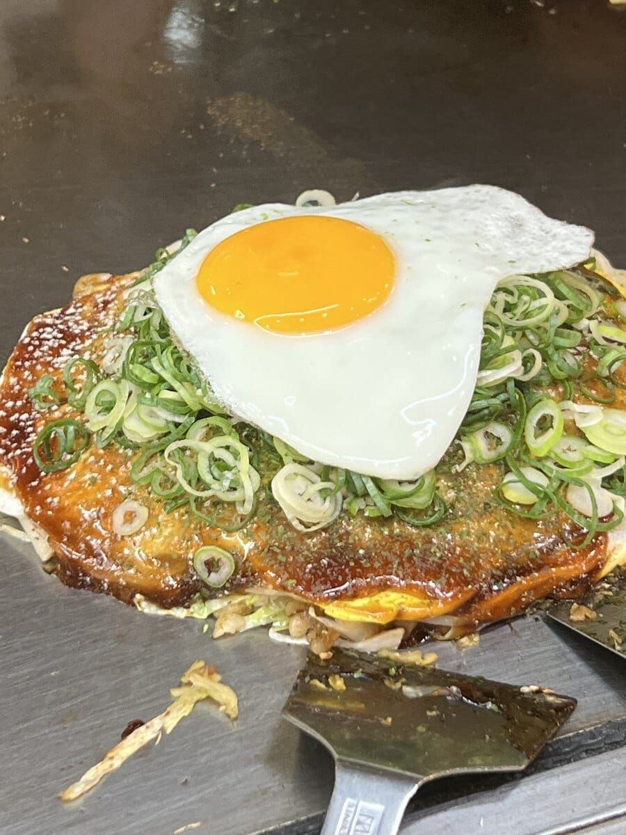 Hiroshima-style okonomiyaki on a hot plate with egg and green onion