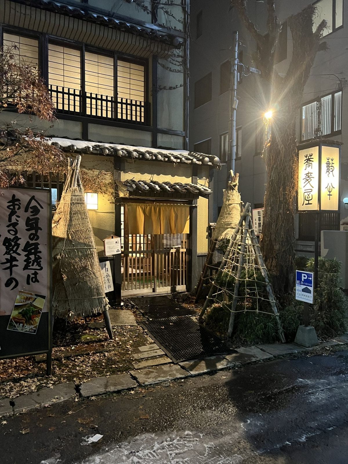 Traditional Japanese ryokan entrance at night with glowing lanterns and a yellow noren curtain in winter
