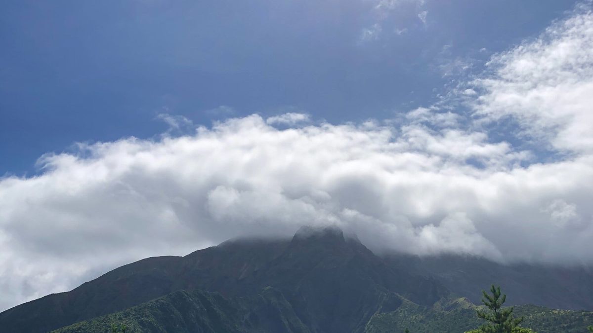 Sakurajima volcano partly covered by clouds beneath a bright blue sky