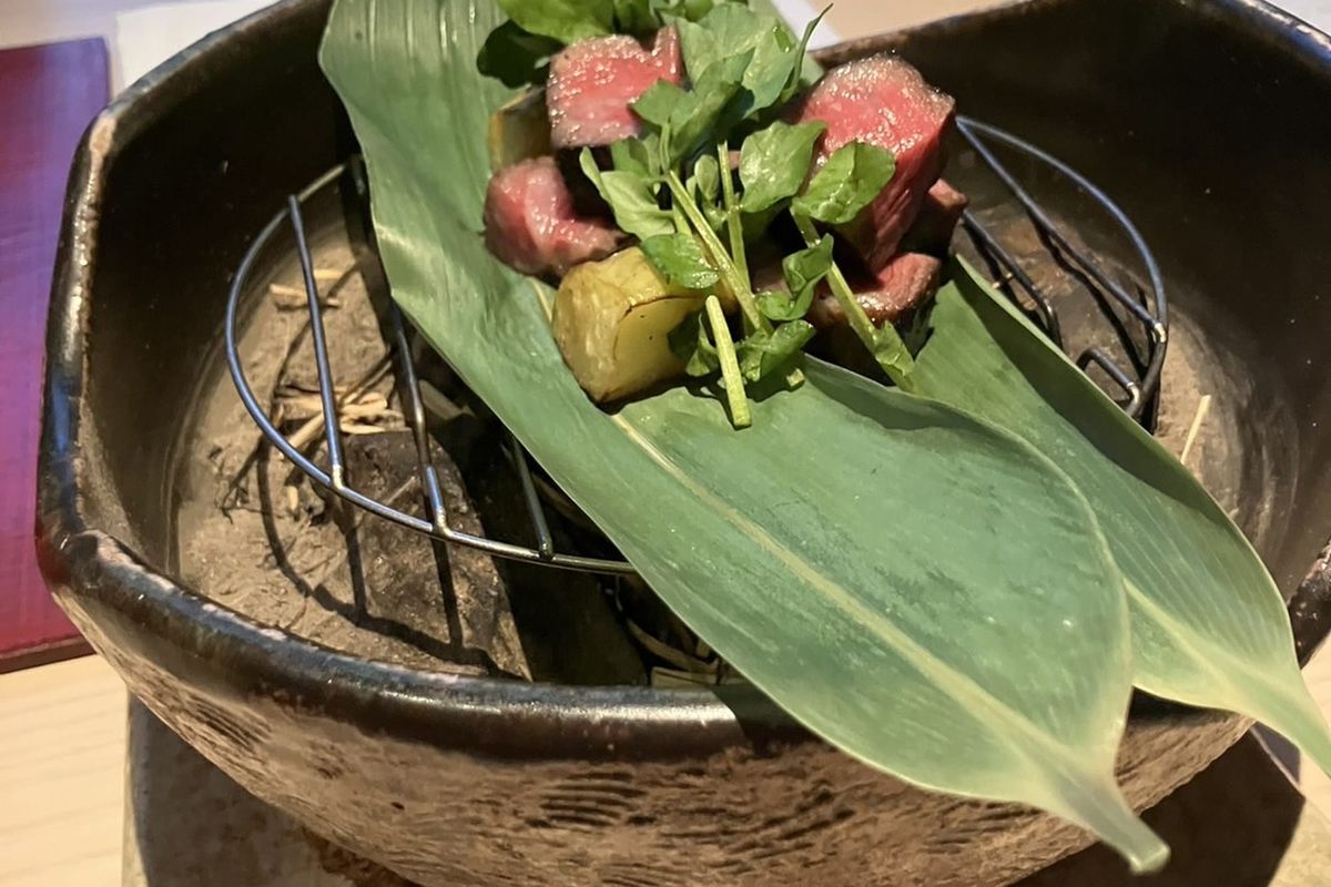 A kaiseki course served on a bamboo leaf in a dark lacquered bowl, garnished with a flower
