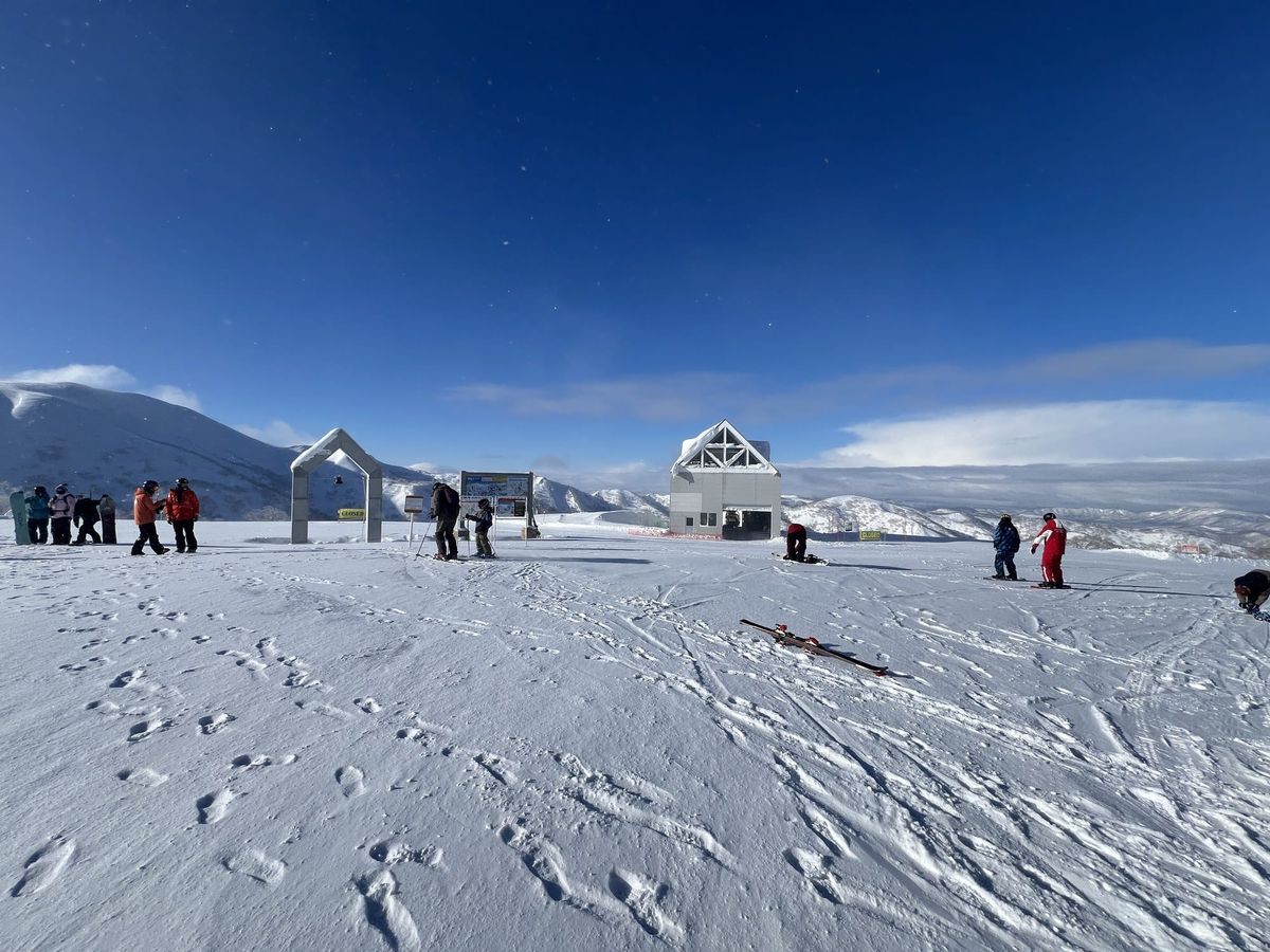 Trail map board and gondola top station at Kiroro under a blue sky