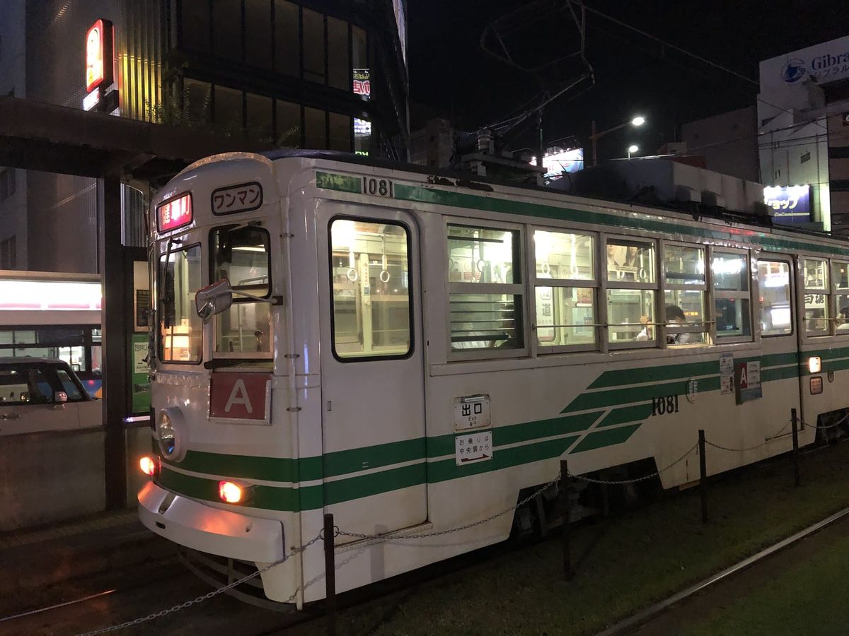 Kumamoto City Tram car at a stop at night with shop signs behind