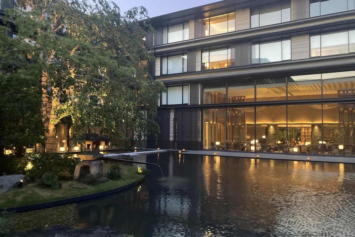 The courtyard garden and pond at HOTEL THE MITSUI KYOTO at dusk, with the lit guest room floors behind it