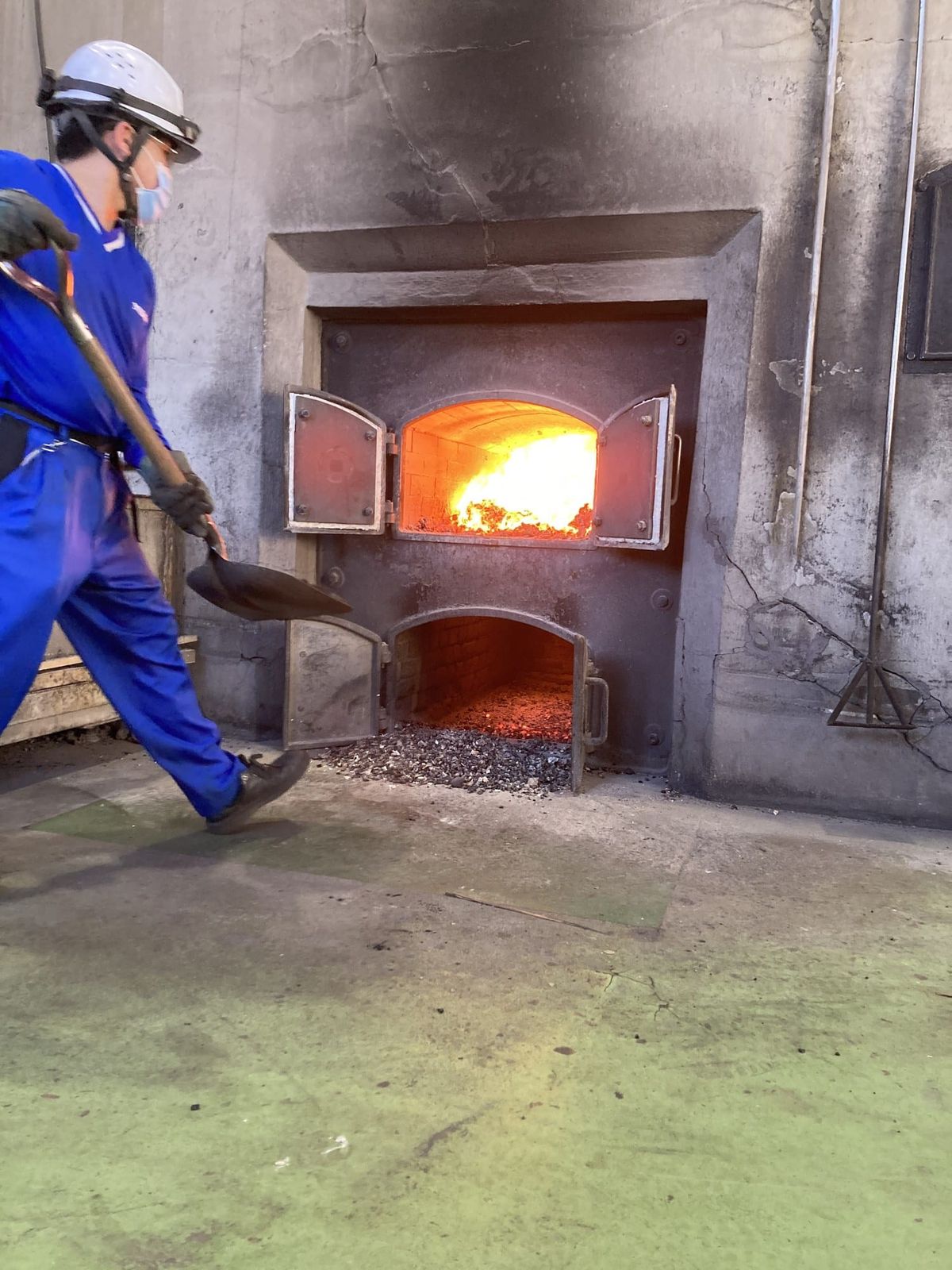 Distillery worker shoveling coal into the lit kiln of a pot still at Nikka Yoichi