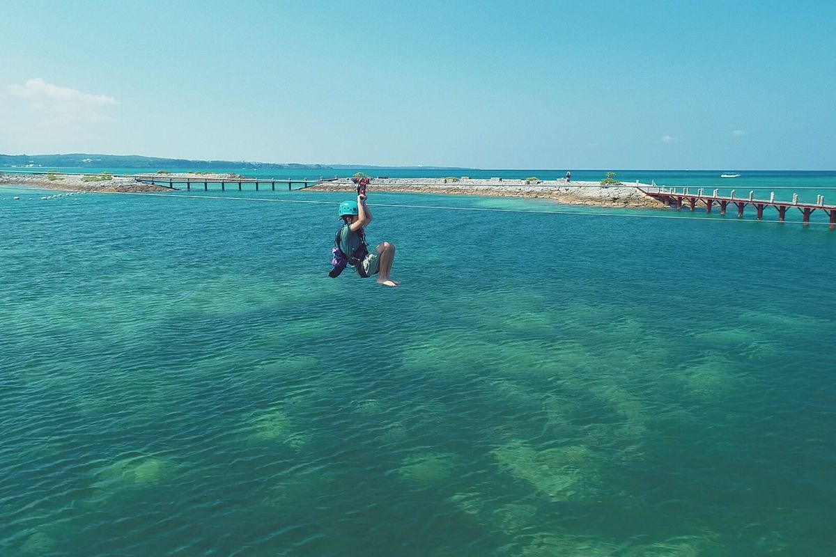 Clear turquoise water over a reef in Okinawa with a long pier running out from the shore