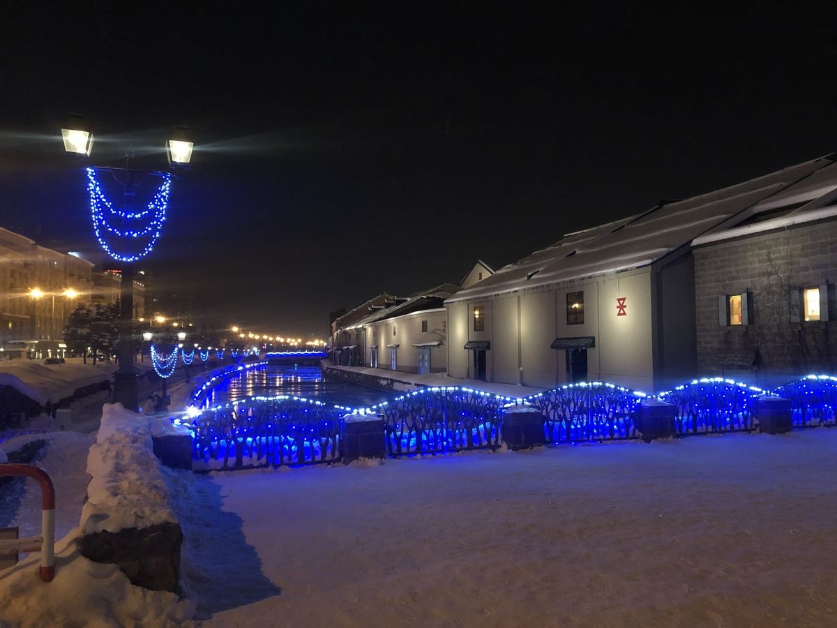 Otaru canal warehouses lit blue at night with snow along the promenade