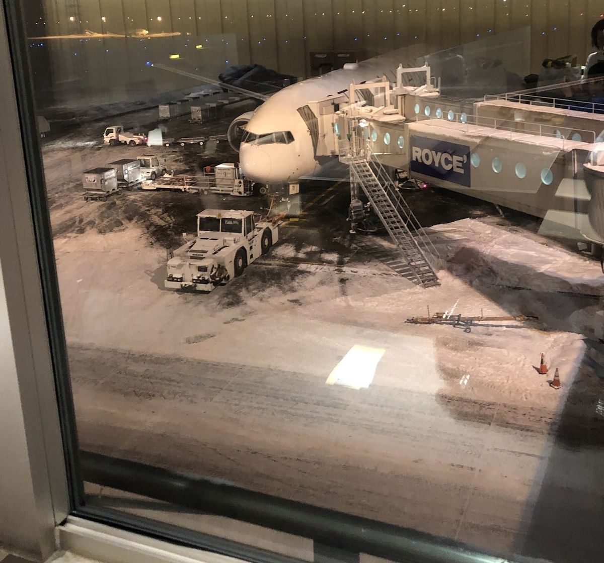 A Boeing 787 at a jet bridge on a snow-covered stand at New Chitose Airport at night