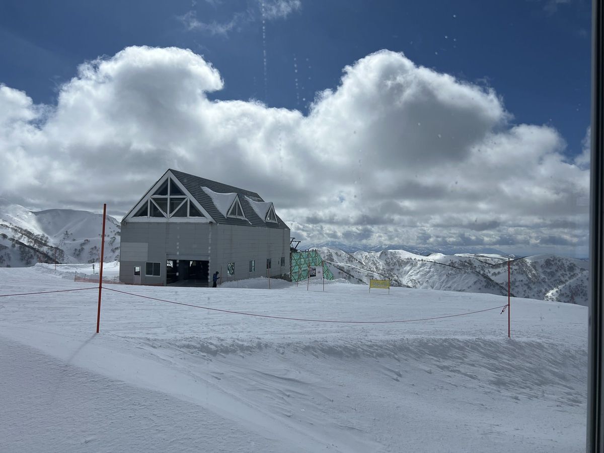 A lift station building at the top of a groomed piste under cumulus cloud