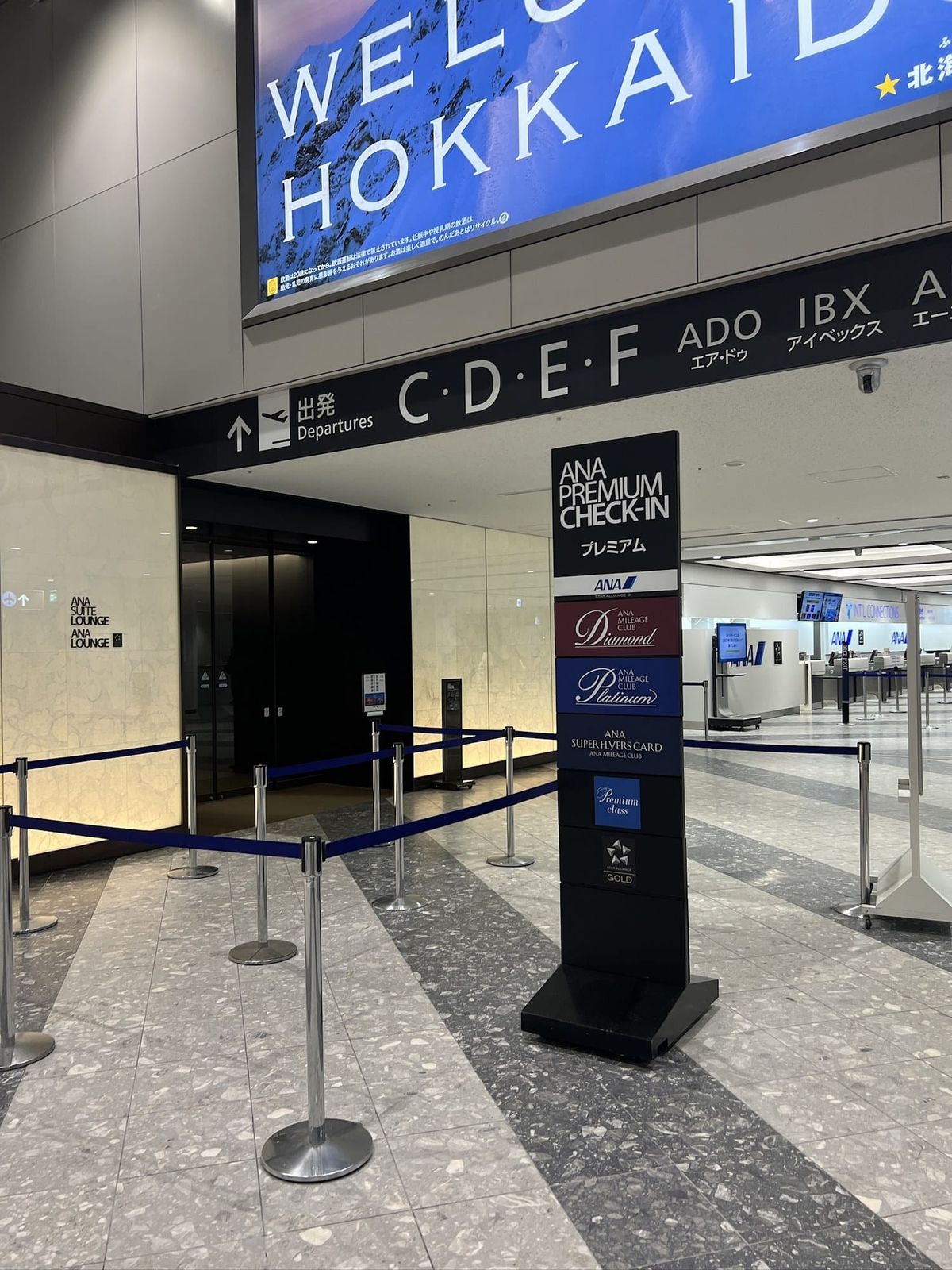 Signage for domestic departure gates C to F at New Chitose Airport beneath a Welcome Hokkaido banner