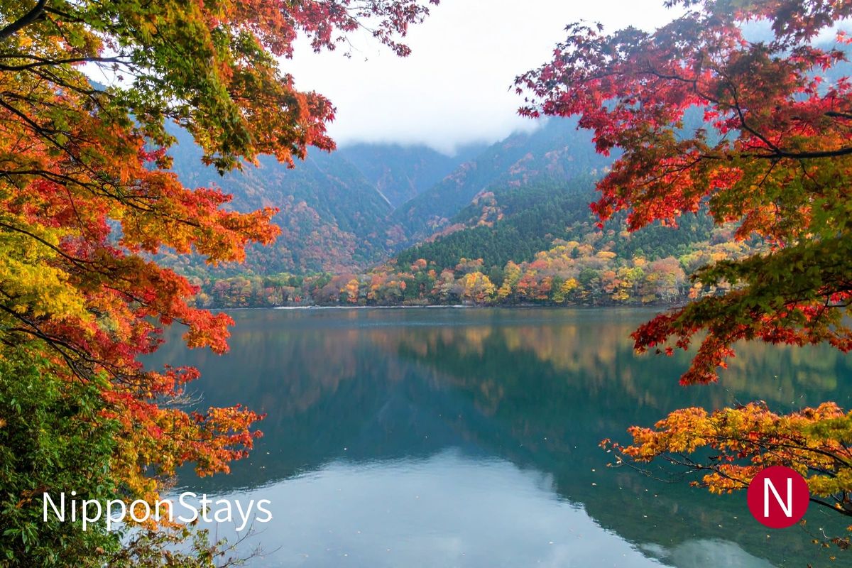 A mountain lake ringed with red and orange trees under low cloud
