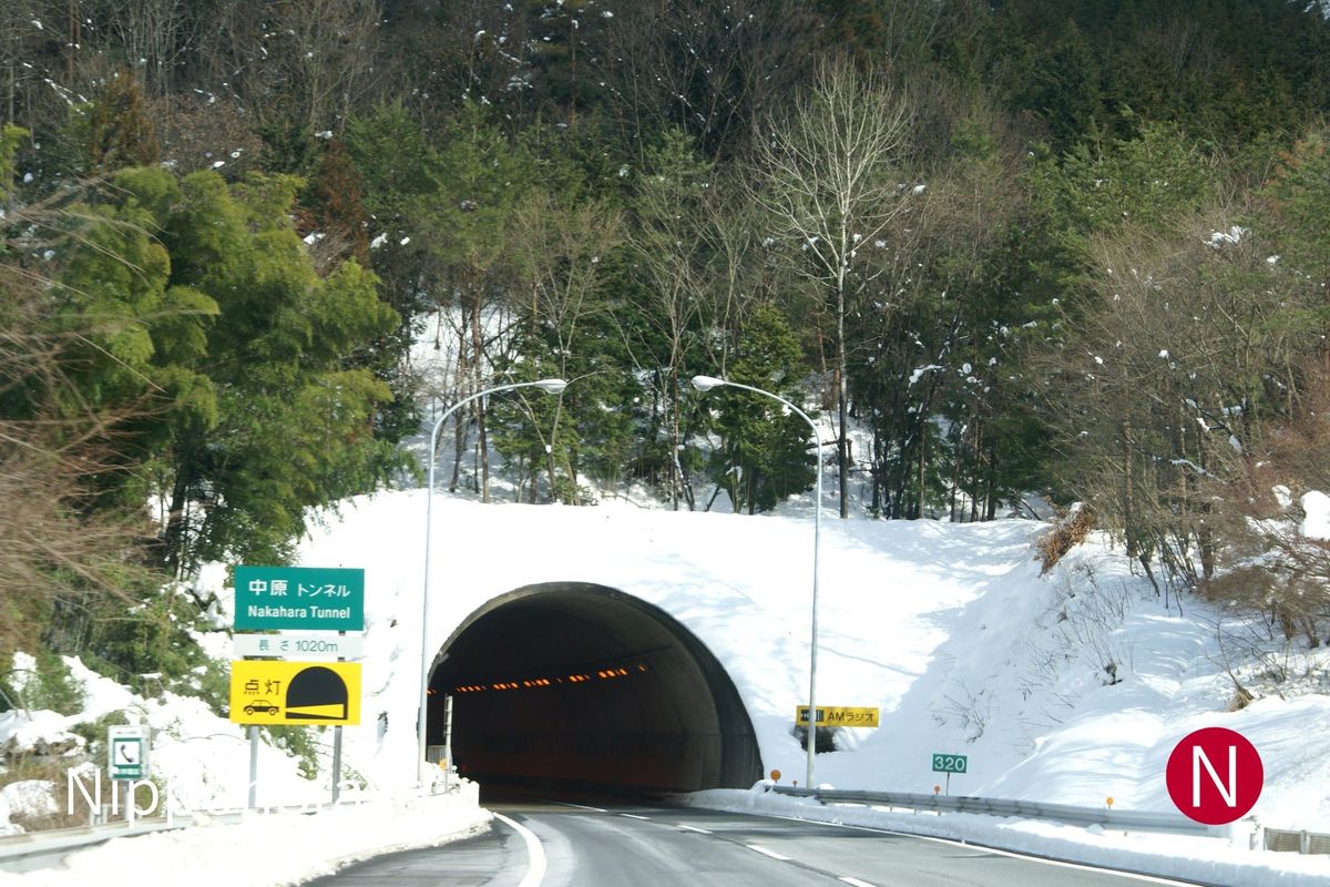Snow-covered mountain road running into a tunnel portal in winter