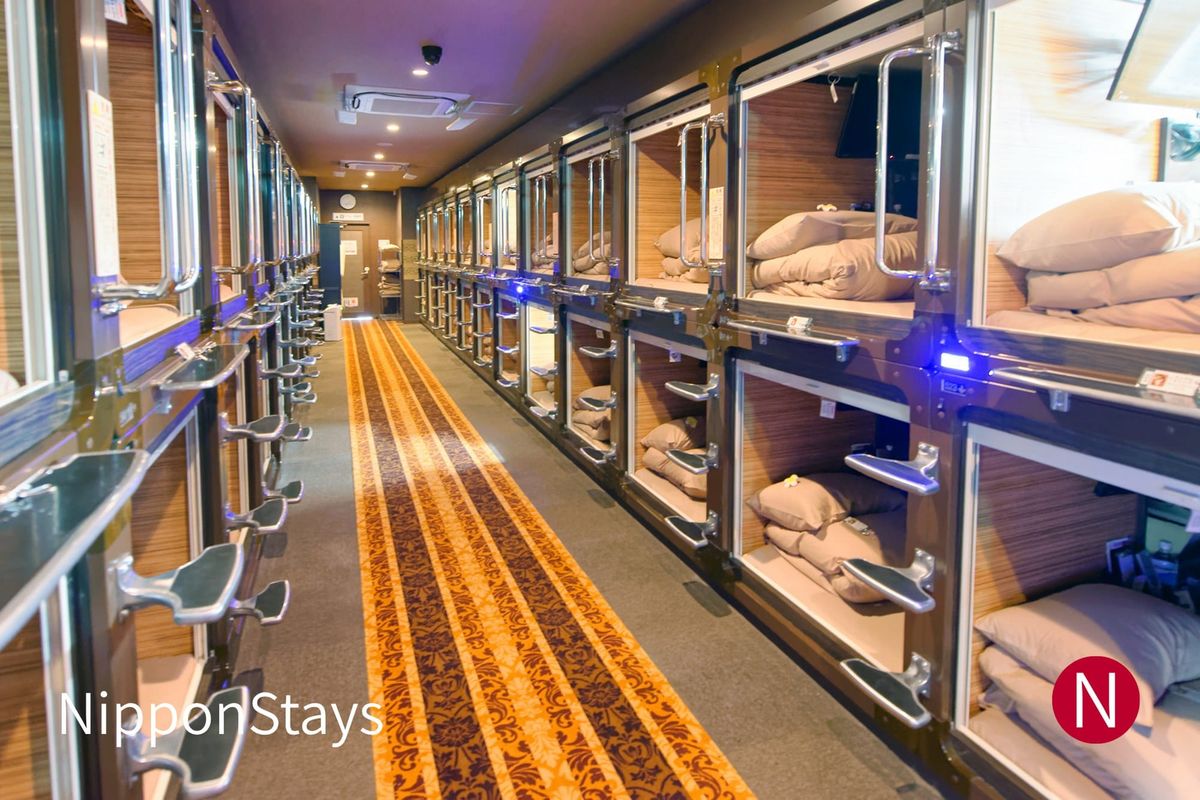A capsule hotel corridor with stacked sleeping pods on both sides