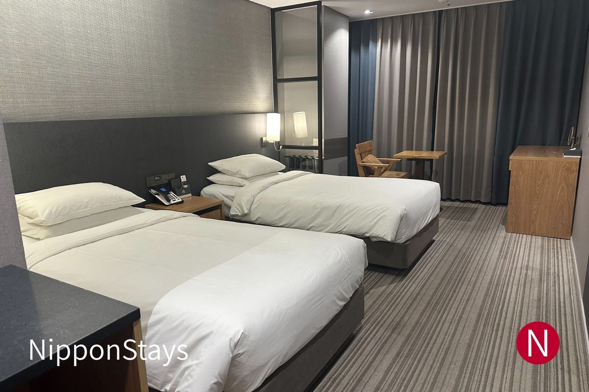 A modern hotel room with two beds and a window