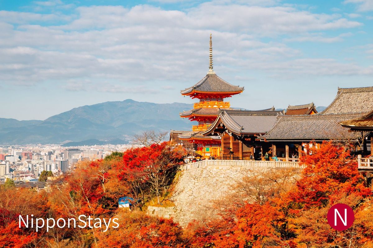A three-storey pagoda and temple hall standing above red maples, with a city spread out below