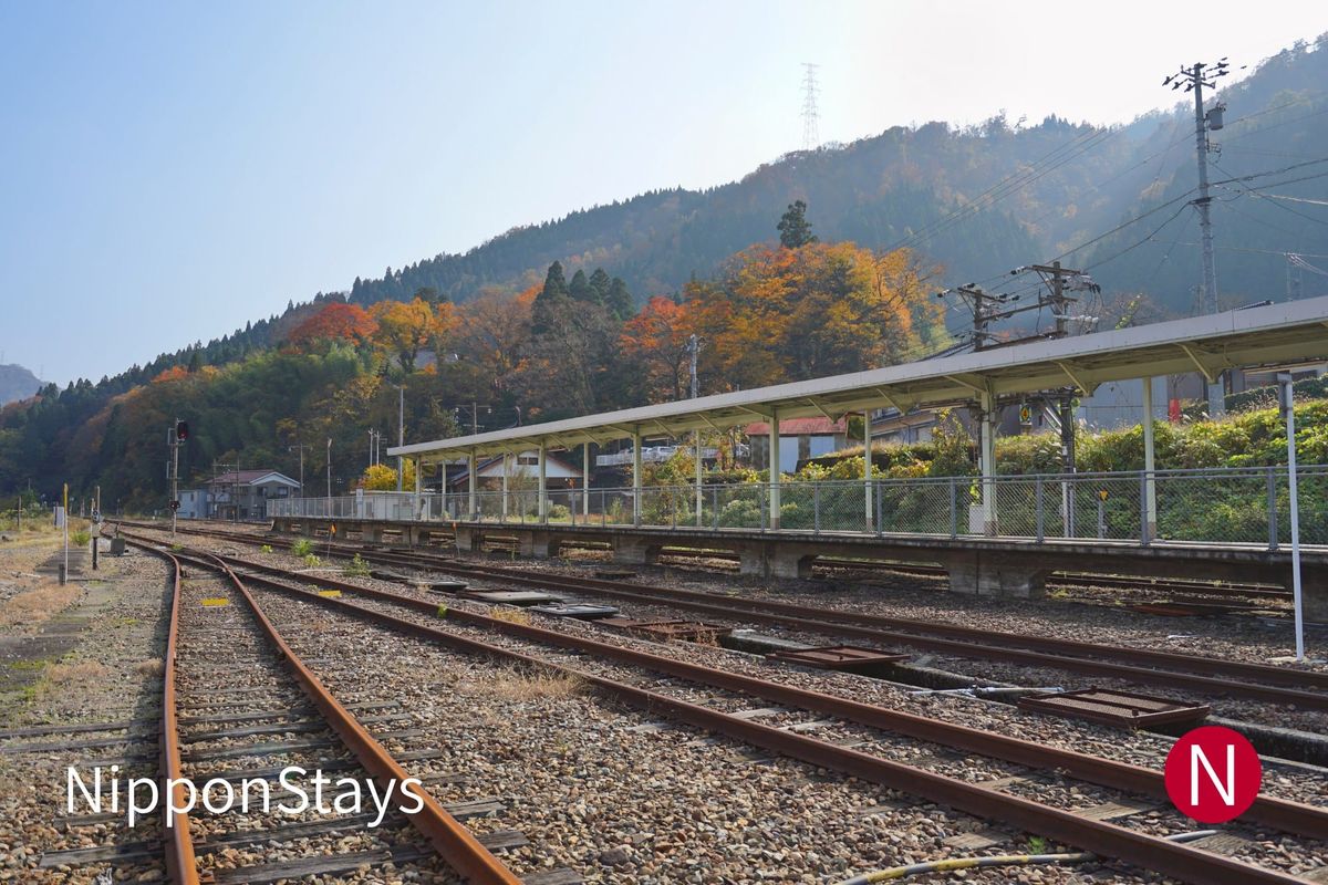 An empty rural station platform and tracks with autumn-coloured hills behind