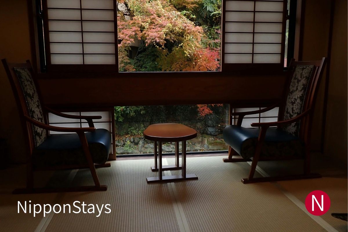 A tatami room with two low chairs facing a window onto a maple garden