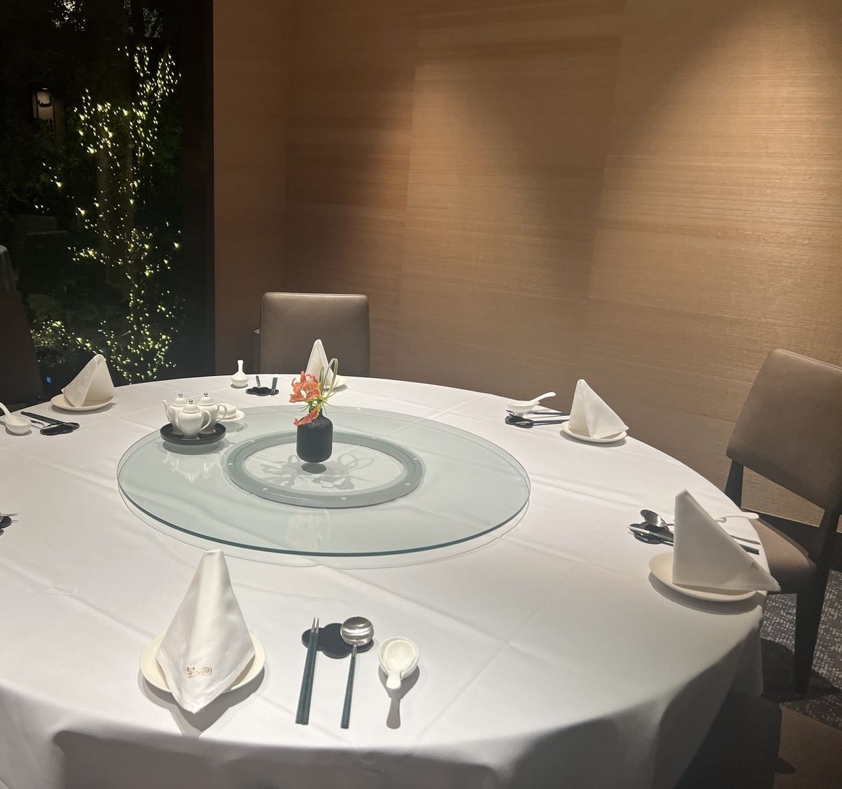 A round table set with a turntable at Star Hill, The Capitol Hotel Tokyu, with the lit garden visible through the window
