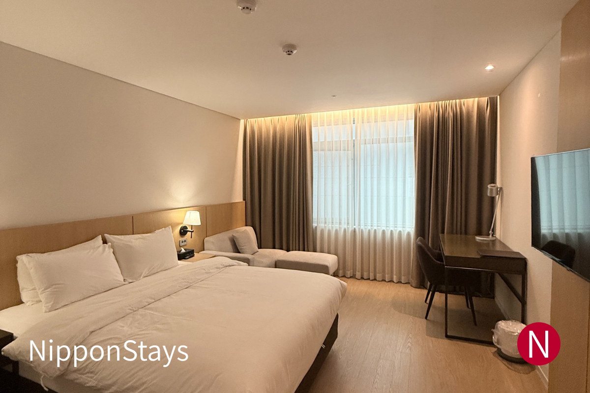 An empty modern hotel room in Japan with a bed, desk and window.