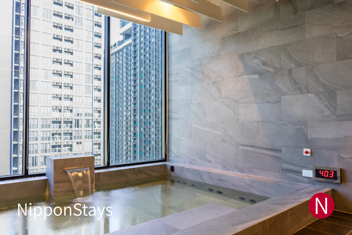 An empty hotel onsen bath with natural stone and warm water.