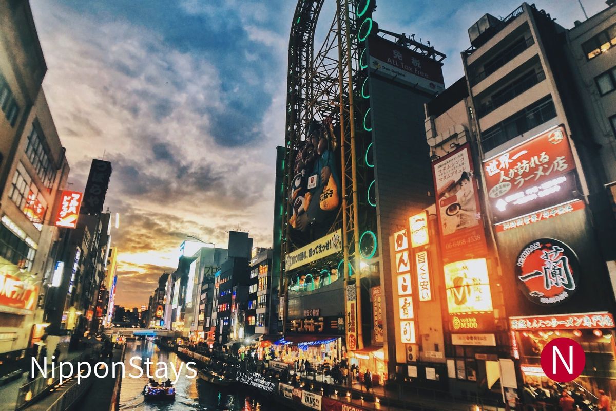 Dotonbori canal at dusk with a ferris wheel and illuminated restaurant signs above the water