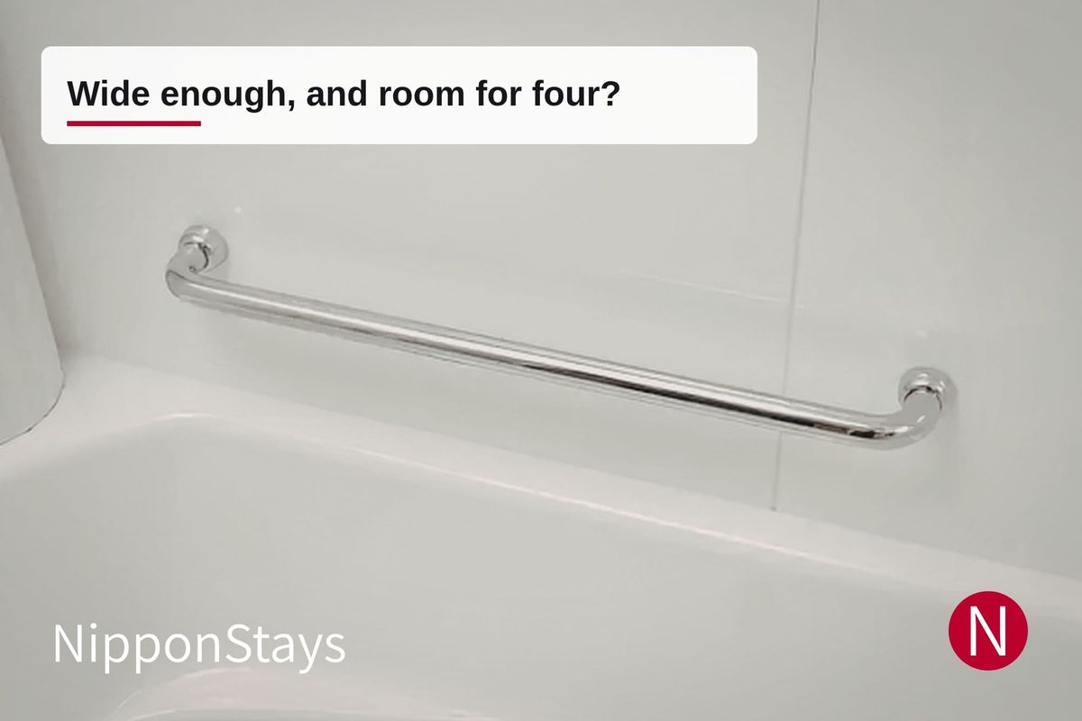 A stainless steel grab bar fixed to the wall beside a white bathtub