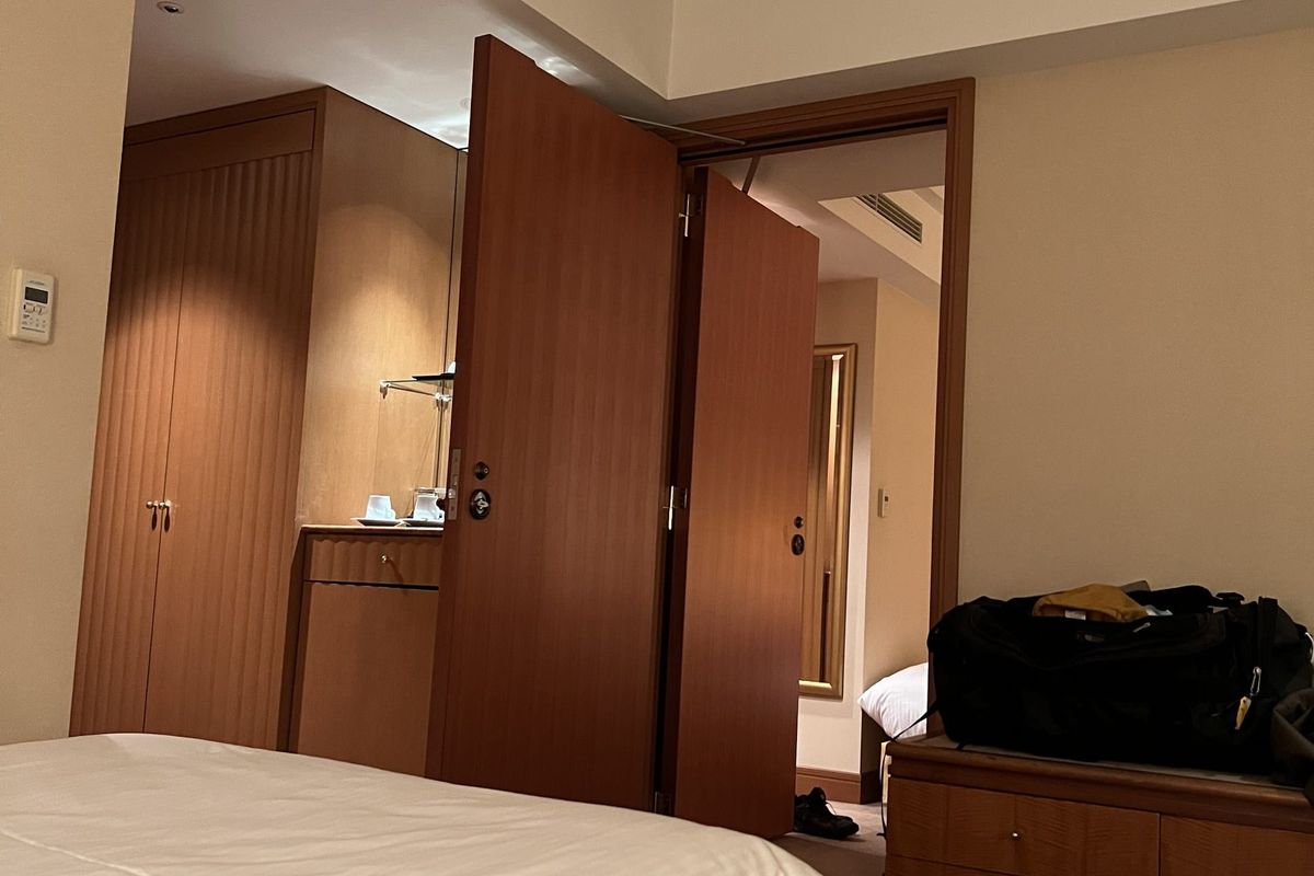 A connecting door opened between two hotel rooms, with both door leaves swung back and the bed of the second room visible through the doorway