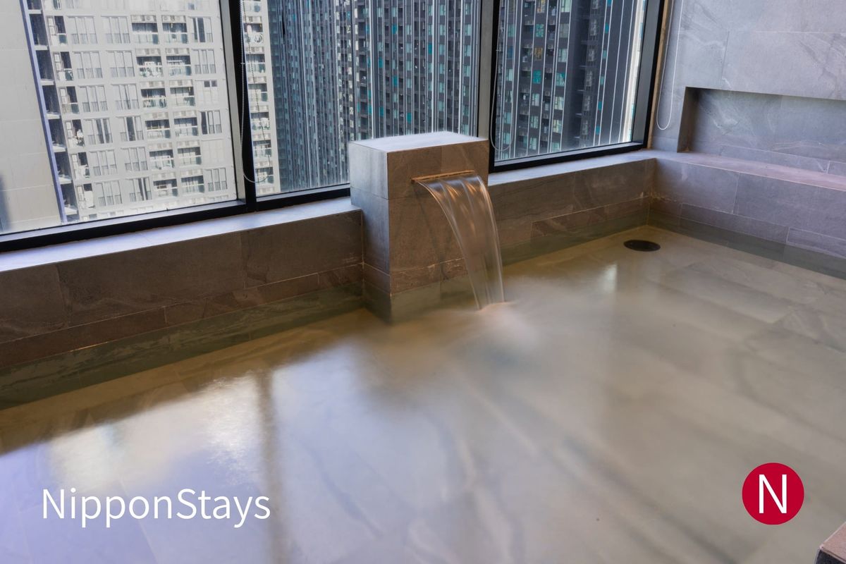 Hotel public bath with a stone spout pouring into the tub beside floor-to-ceiling windows