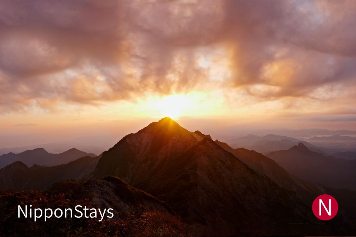 The sun rising behind a sharp mountain peak above a sea of clouds, seen from a summit