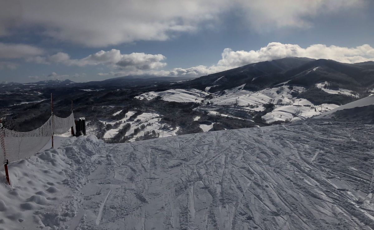 A safety net on red poles running along the edge of a groomed run at a Hokkaido ski area, with the valley and neighbouring pe