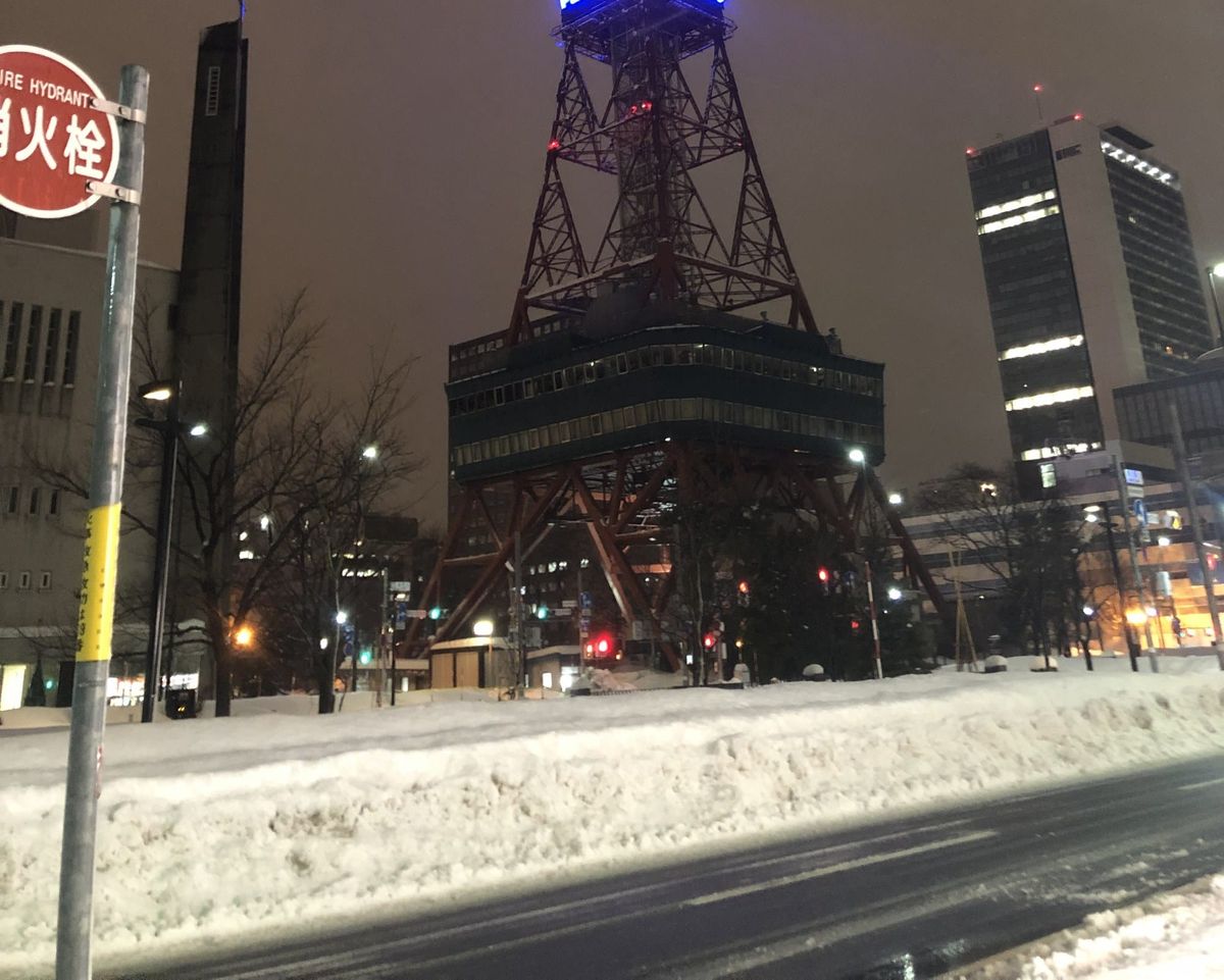 Sapporo TV Tower lit at night above a plowed snowbank beside a cleared street