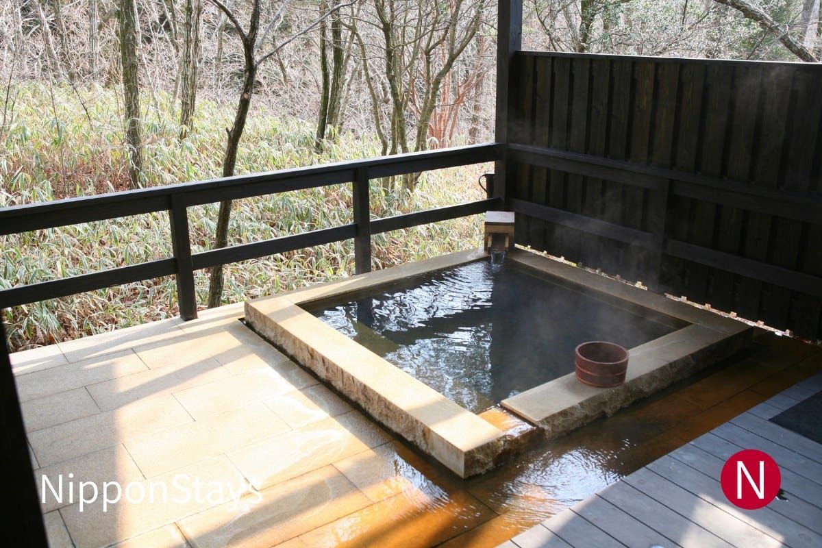An open-air stone bath at a Japanese inn, steaming, with no bathers present