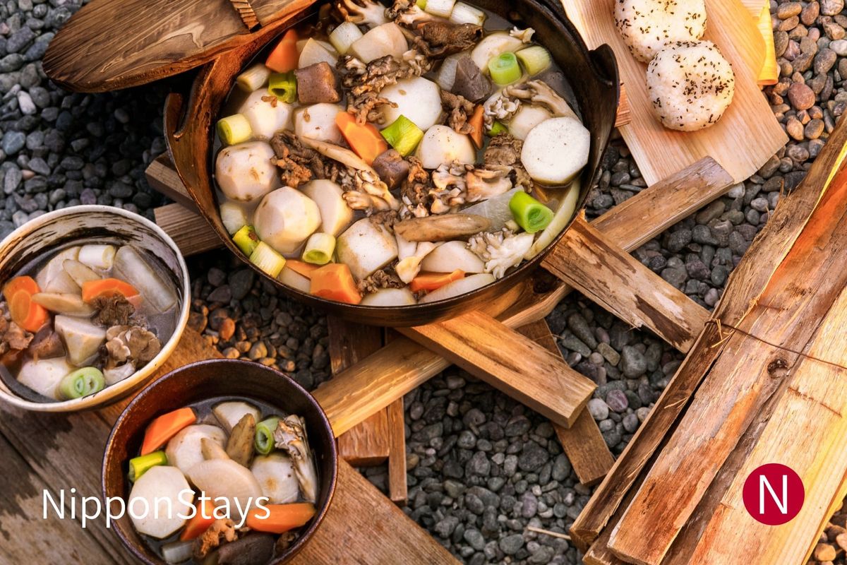 A pot of imoni with taro, mushrooms and carrot cooking beside a riverbank