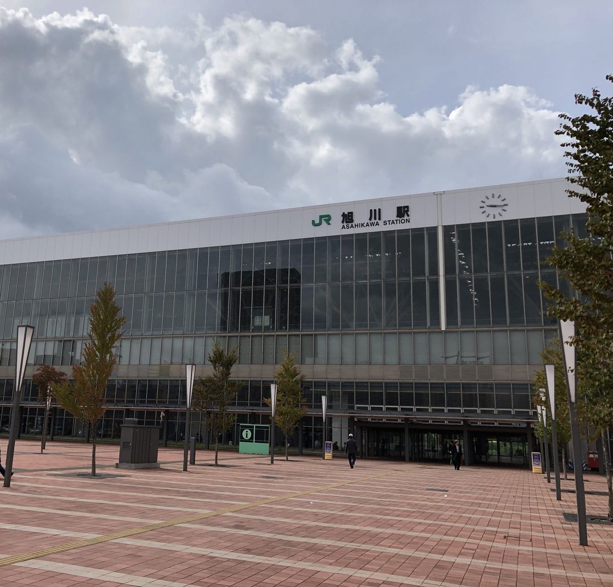 The glass facade of JR Asahikawa Station in Hokkaido under a cloudy sky, seen from the brick station square