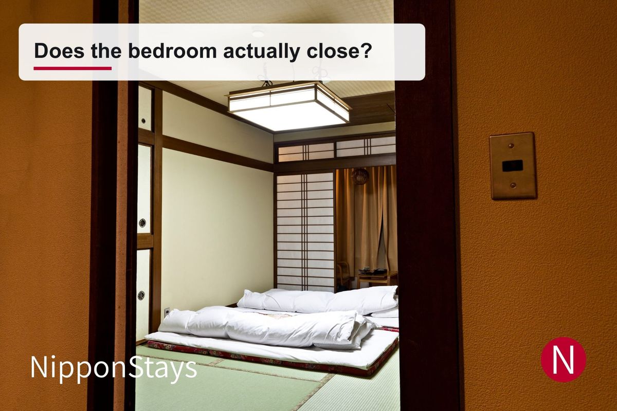 A tatami room with futon laid out, seen through a wooden doorway from the next room
