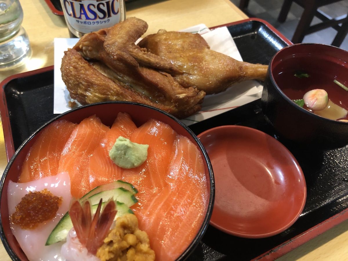 Half-fried chicken, a seafood rice bowl and a bottle of Sapporo Classic on a table at Naruto in Otaru