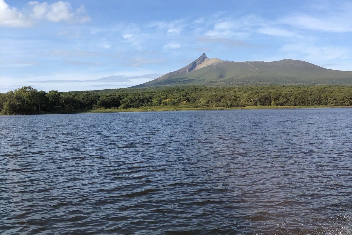 Mount Komagatake rising above the forested shore of Lake Onuma, seen from a boat on the lake
