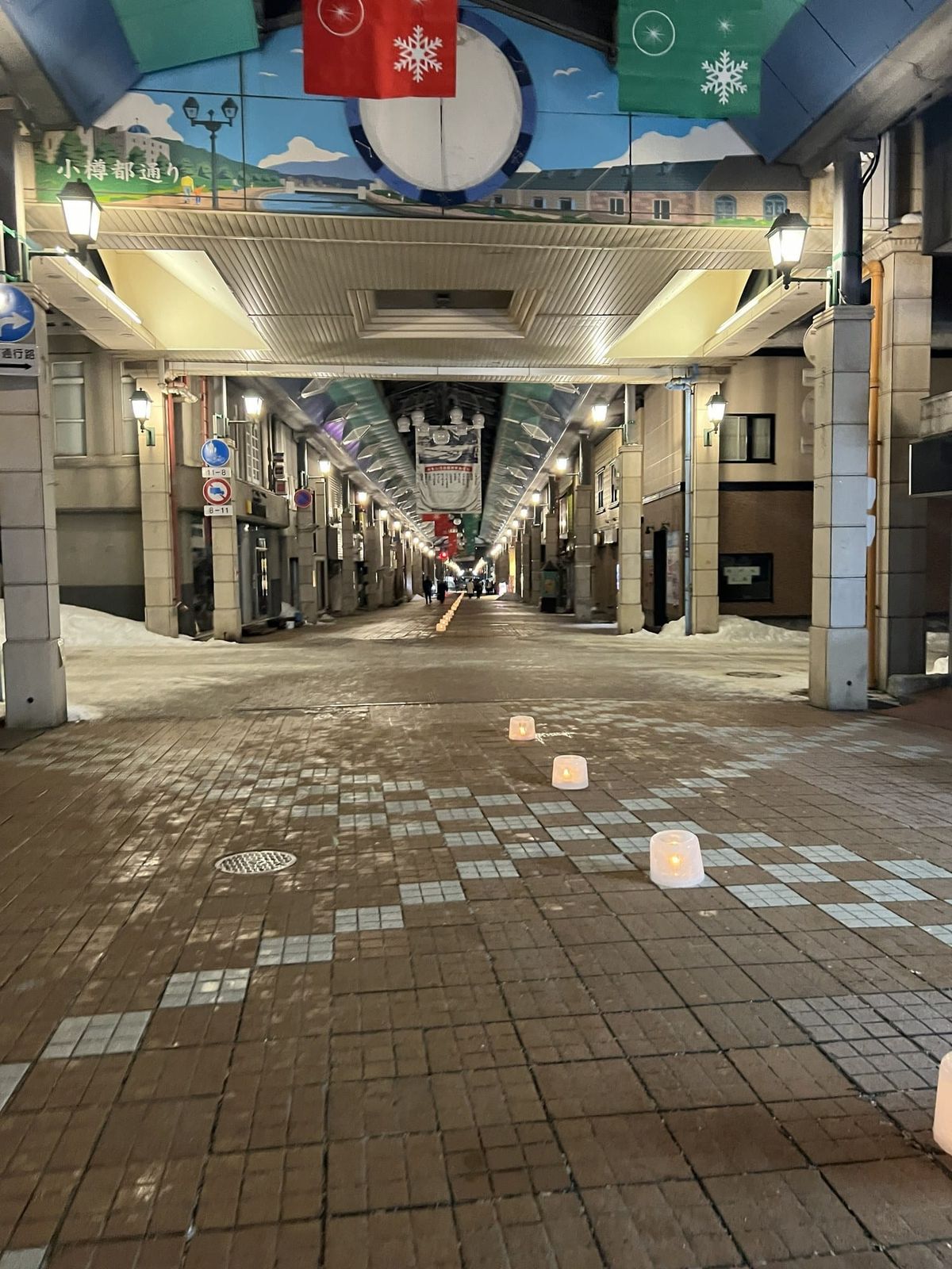 Small ice-candle lanterns lined up down the middle of the Miyakodori shopping arcade in Otaru at night, with snow piled at the edges