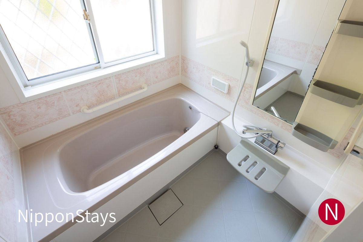 A Japanese bathroom with a tub, a tiled washing area, a hand shower and a stool