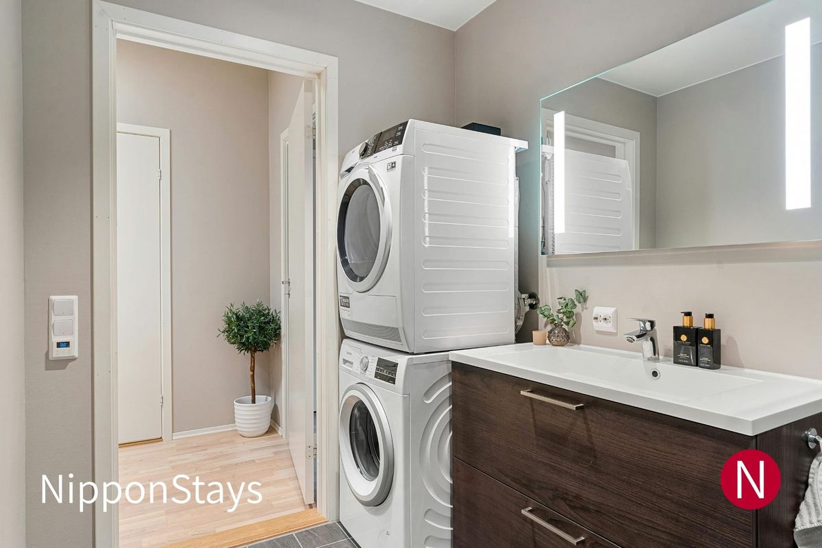 A stacked washer and dryer beside a bathroom vanity in a hotel-style room