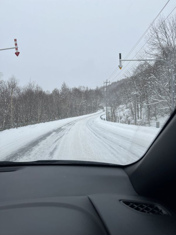 Snow-packed road toward Kiroro seen through a windshield, with red-and-white arrow markers overhead