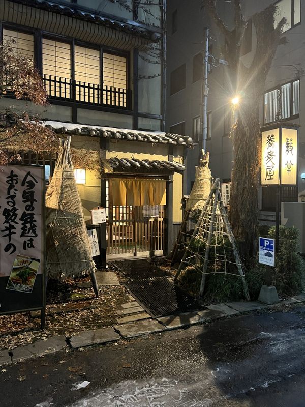 Traditional Japanese ryokan entrance at night with glowing lanterns and a yellow noren curtain in winter
