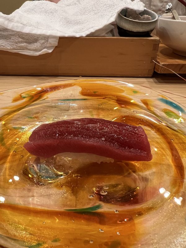 Single piece of tuna nigiri sushi served on a hand-blown glass plate at an Otaru sushi counter