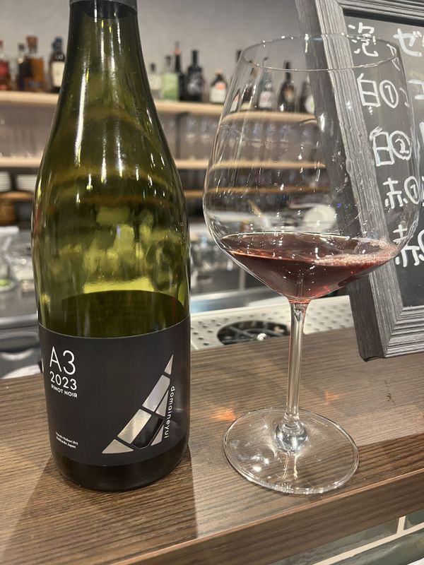 A glass of red wine and a bottle of Domaine Yui A3 2023 on a Yoichi wine bar counter