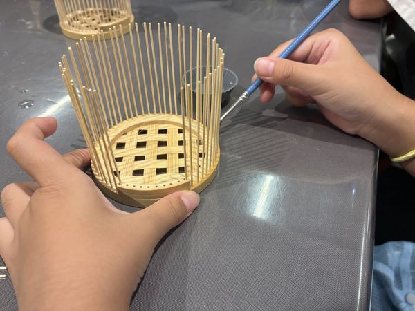 A child's hands setting fine bamboo ribs into the base of an insect cage at a workshop in Aoyama, Tokyo